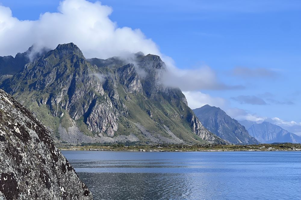 Grønn fjellside med skyer over fjorden om sommeren