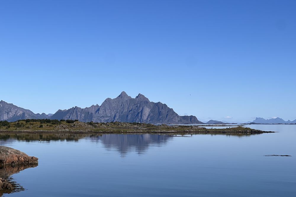 Fjell som speiler seg i blikkstille sjø en sommerdag